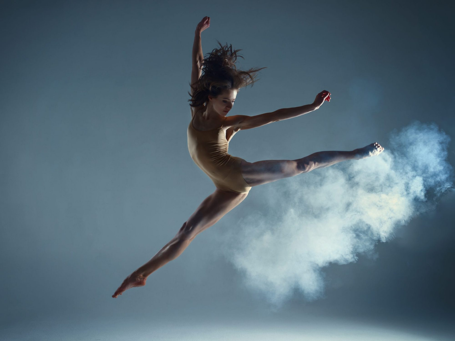 Dancing in cloud concept. Muscle brunette beauty female girl adult woman dancer athlete gymnast in smoke fog wearing dance bodysuit jumping in mid air, performance on isolated grey / black background